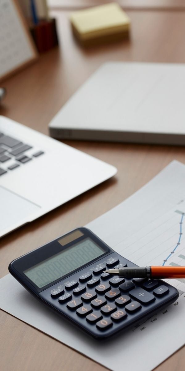 Calculator and Paper with Pen and Laptop in the Background