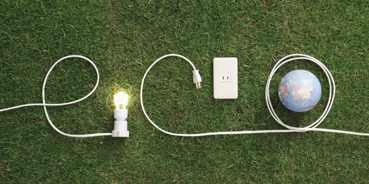 A lawn with cords and a lightbulb wrapped around the world representing energy efficiency