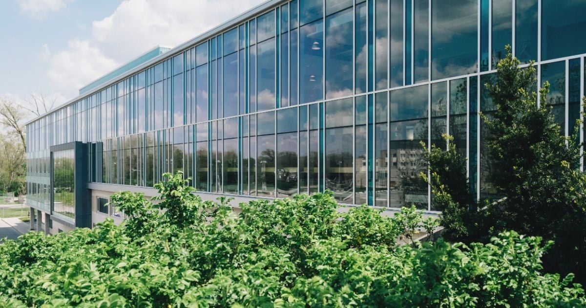 Modern commercial office building with large reflective glass windows and green landscaping, representing energy-efficient design and HVAC upgrade potential.