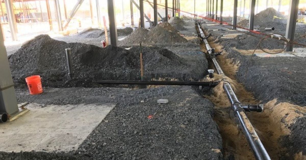 Commercial plumbing installation in progress with exposed piping and trenching inside a steel-framed building in Rhode Island.