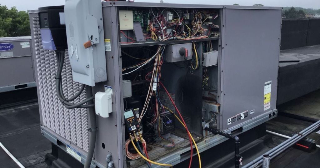 Open commercial rooftop HVAC unit under repair with diagnostic tools and wiring exposed during emergency service.