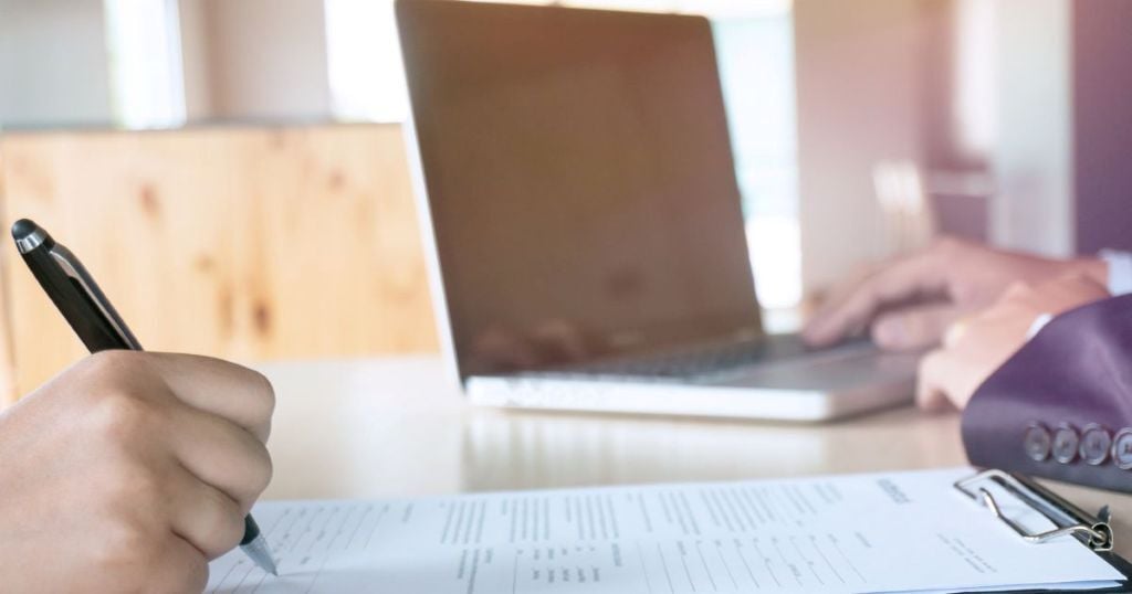 Someone filling out an application with interviewer in the background