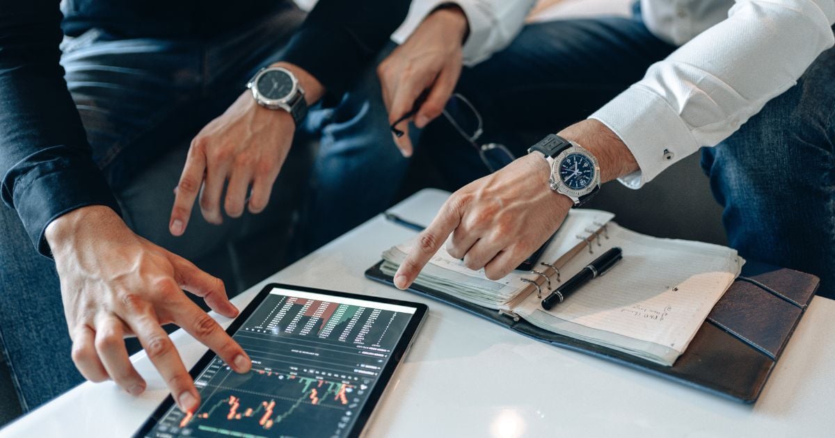 Tablet with graph on desk with two people pointing at it