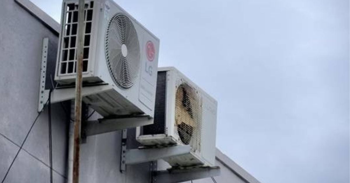 Two outdoor wall-mounted HVAC condenser units, one LG-branded and the other older and rusted, installed on the exterior of a commercial building against a cloudy sky.