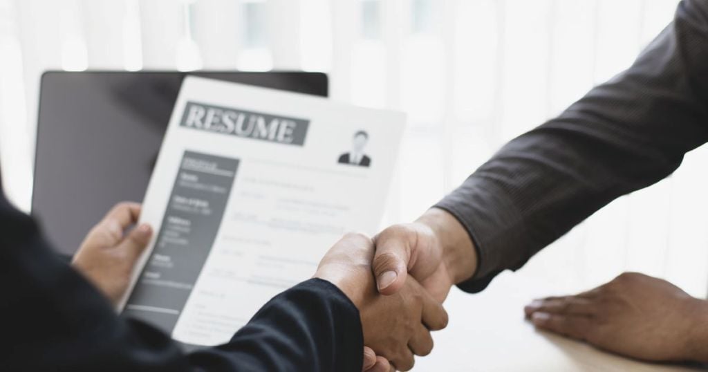 Two people shaking hands with a resume
