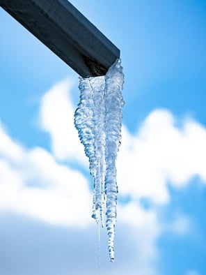 Icicle hanging off a pipe representing cold weather