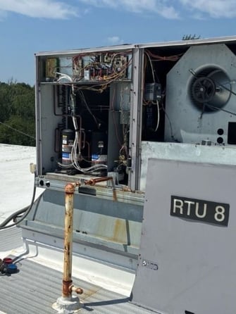 Open rooftop HVAC unit undergoing preventative maintenance, showing internal components being inspected and serviced.