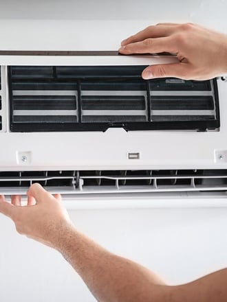 HVAC Technician fixing small AC unit inside an apartment. Representing how maintenance is important for a commercial building.