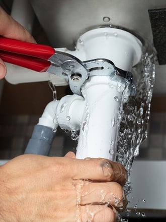 Plumber fixing a leaking pipe, representing a commercial building plumbing emergency