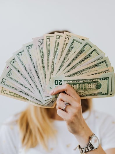 Woman holding a fan of money, representing saving money from preventing costly breakdowns of an HVAC system