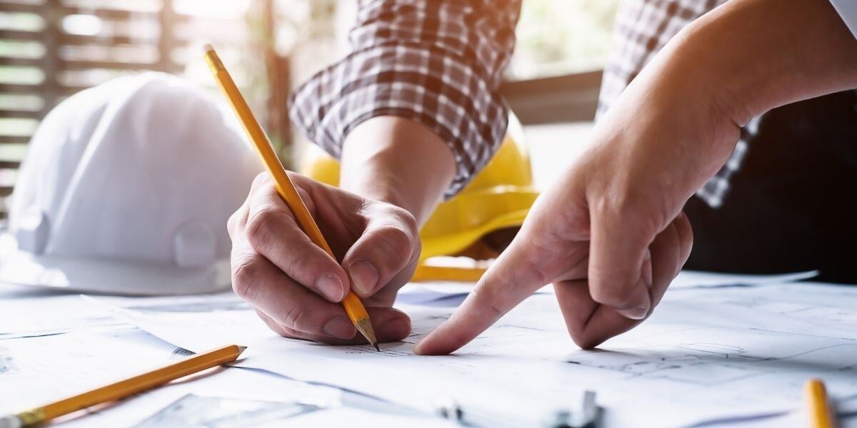 Person pointing to a plan and another person writing on plan with pencil