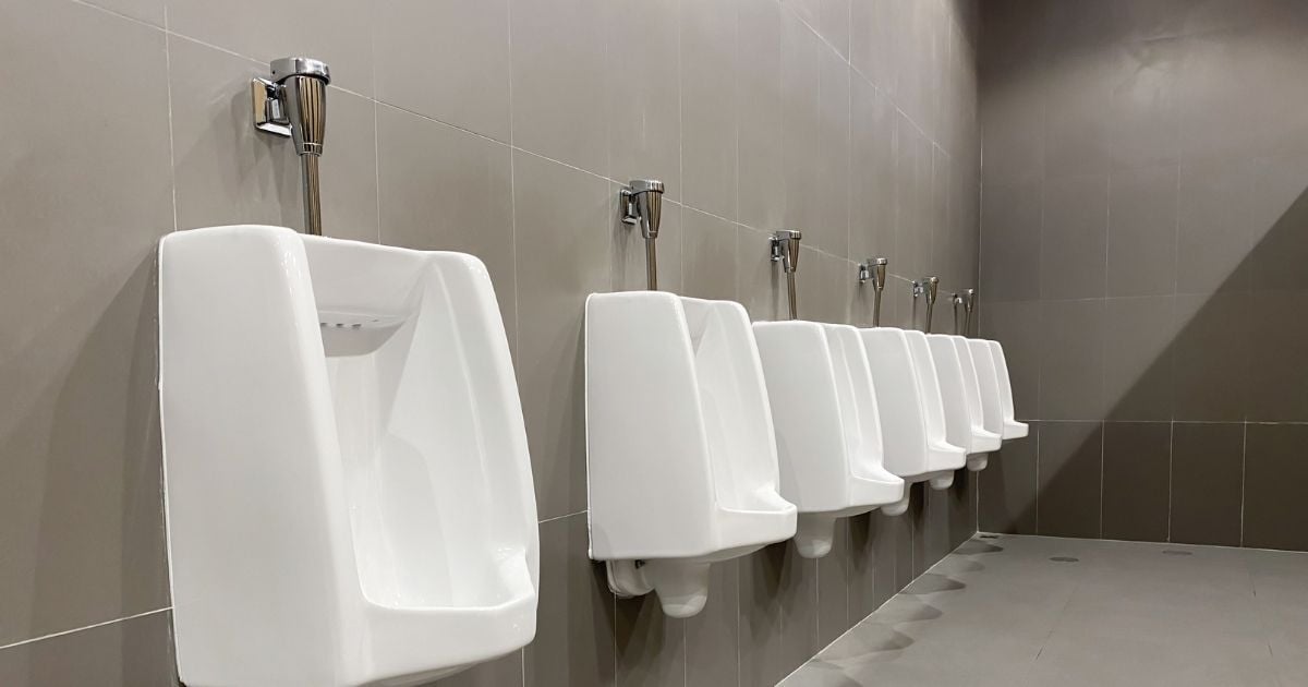 Row of wall-mounted commercial urinals in a clean, modern school restroom with gray tile walls.