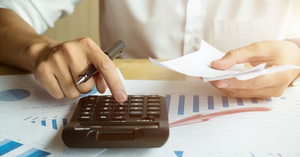 Close-up of a person calculating energy expenses with a calculator, holding utility bills, and reviewing bar charts,representing rising energy costs in Massachusetts in 2025.