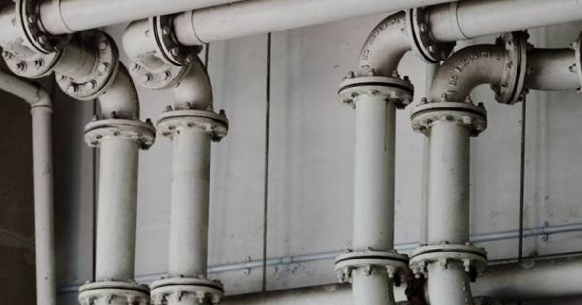 Close-up view of industrial water pipes in a commercial building, showing joints and valves commonly found in school plumbing systems.