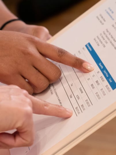 Two people pointing at a printed invoice or cost breakdown on a clipboard, focusing on line items and total amounts.