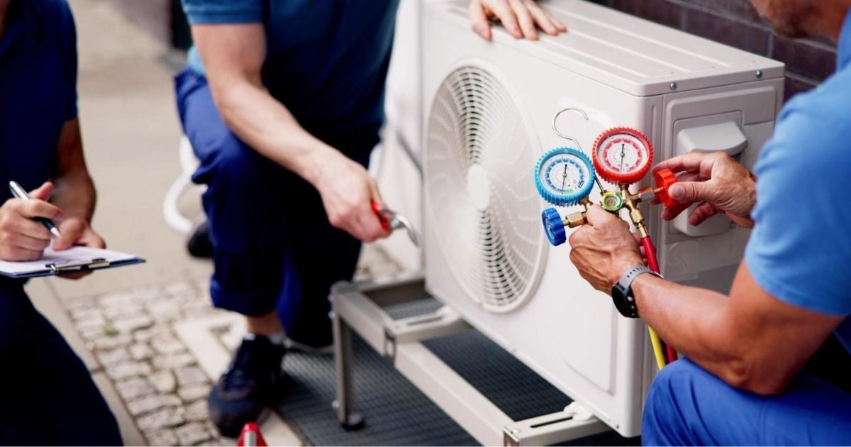 HVAC technicians diagnosing heat pump performance issues using refrigerant gauges on outdoor unit